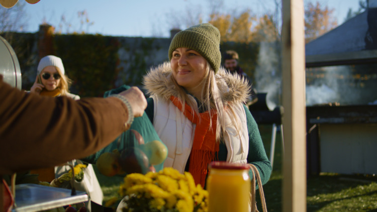 Adult woman chooses apples at the stall with fruits and vegetables on a local farmers market or fair outdoors