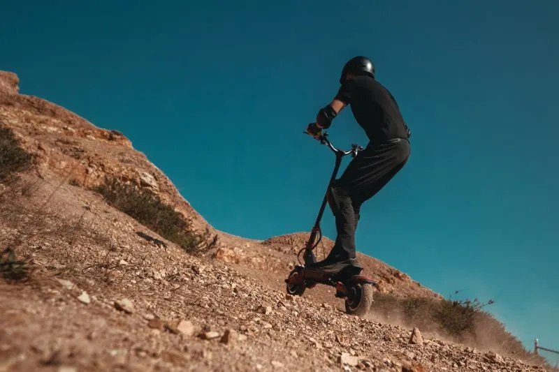 15 Electric Scooters Pros and Cons to Know 10 Man riding an Off-road electric scooter uphill