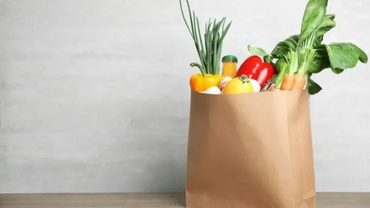 Paper bag with vegetables and bottle of juice on table