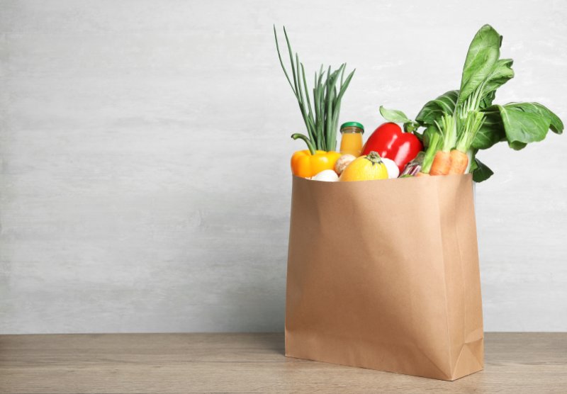 Paper bag with vegetables and bottle of juice on table