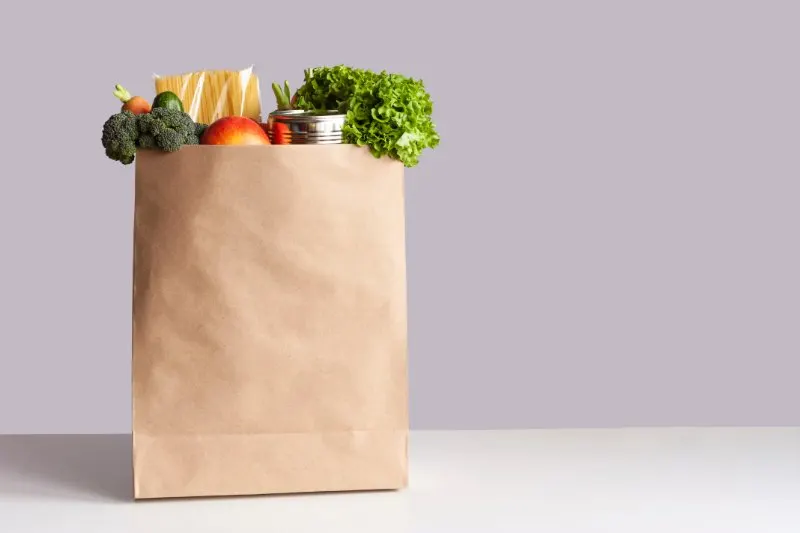 Bag of food with fresh vegetables, fruits, pasta and canned goods
