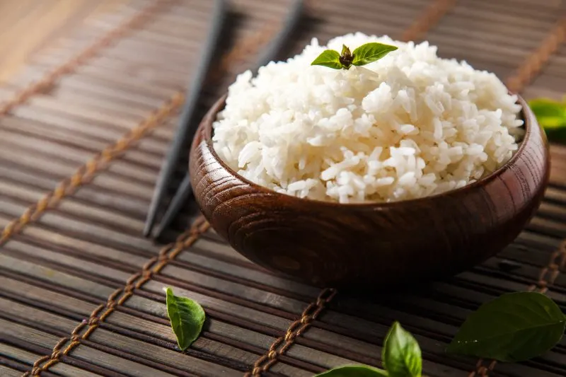 Cooked white rice in dark wooden bowl