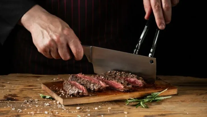 Slicing juicy beef steak by knife in chef hands closeup