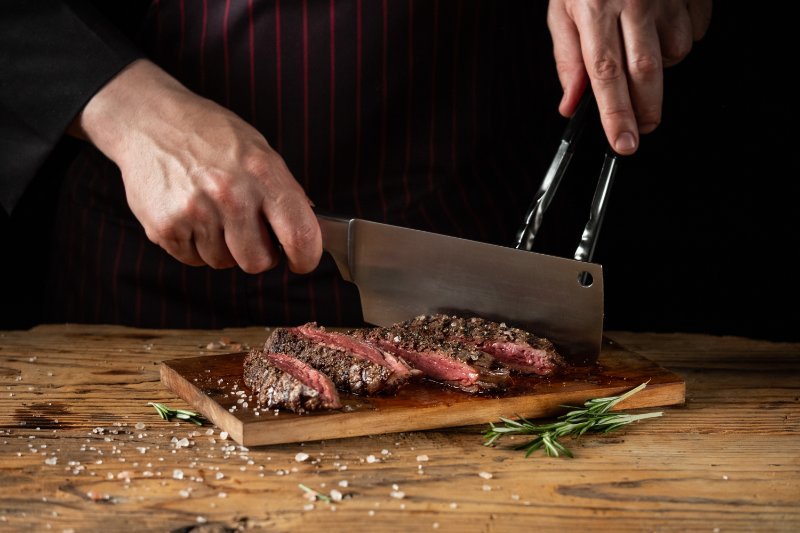 Slicing juicy beef steak by knife in chef hands closeup