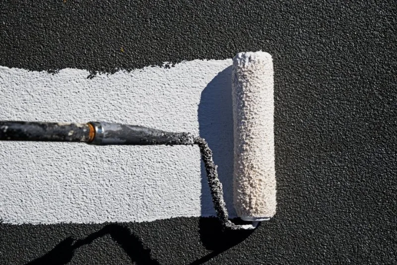 Painter painting the roof with white color using paint brush