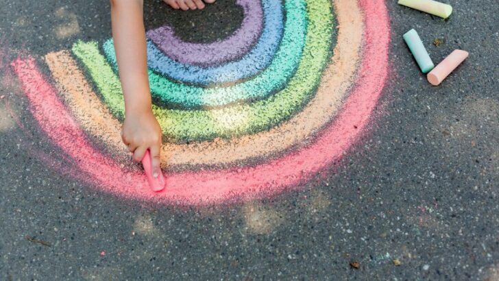 child's drawing rainbow with colorful chalks on a street