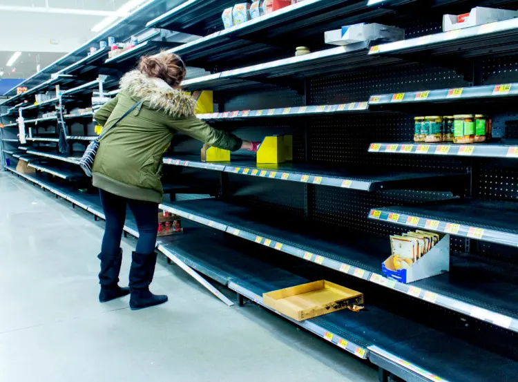 Woman grabbing product of of thinly stocked shelves at a supermarket