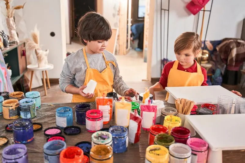 boys standing at the table and looking attentively at the jars with paints
