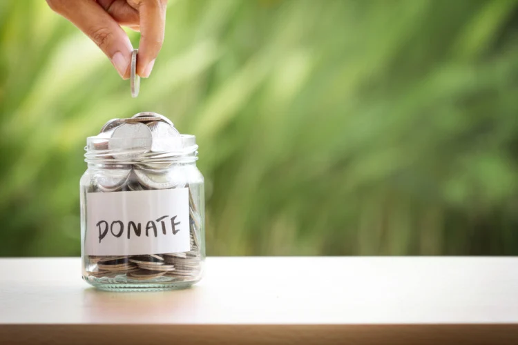Earth Day Checklist: 21 Things to Do on This Day 9 Hand putting Coins in glass jar for giving and donation concept