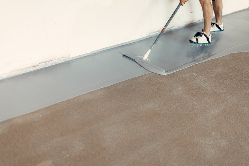 Construction worker apply grey epoxy resin in an industrial hall