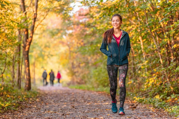 Woman walking in autumn forest nature path walk on trail woods background. Happy girl relaxing on active outdoor activity.