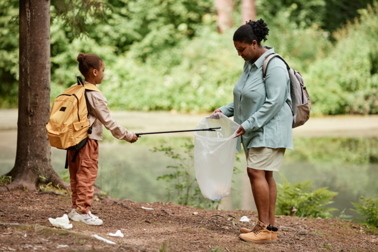 Side view portrait of black mother and daughter helping cleaning nature together and picking up trash by river