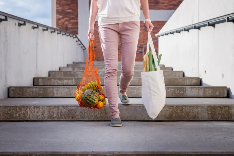 Woman walking at stairs and carrying reusable mesh bag after shopping groceries