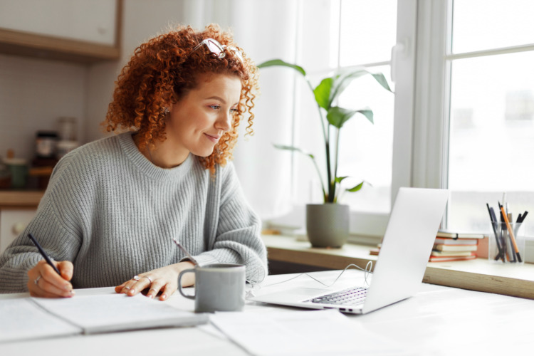 Cute university student with curly red hair doing homework sitting