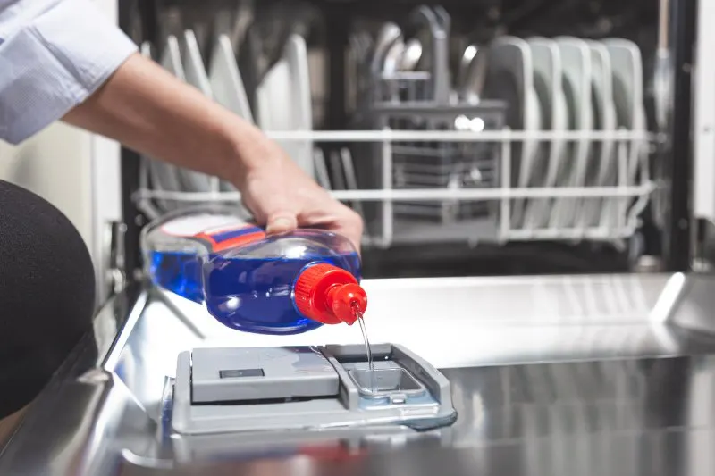 Close-up hand filling dishwasher with gloss liquid into the dishwasher box