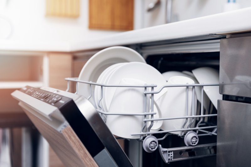 Closeup of open dishwasher with clean dishes, glasses and bowl