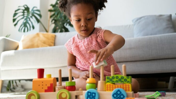 kid playing with colourful wooden railway station at home.