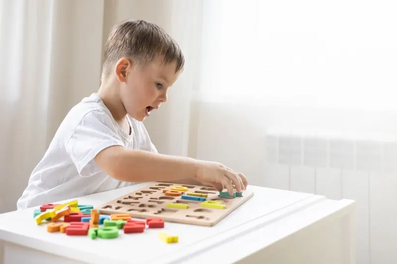 kid playing with wooden alphabet letters board on table top