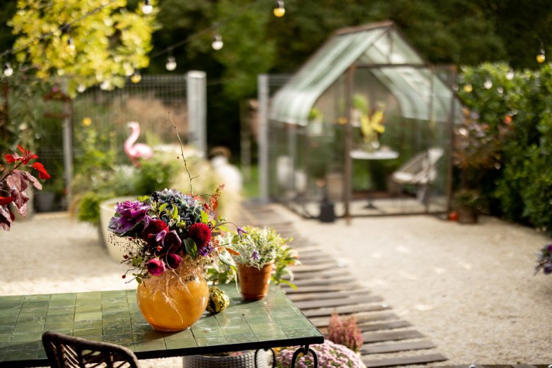 Beautiful bouquet of flowers in vase on the table at backyard with greenhouse on background
