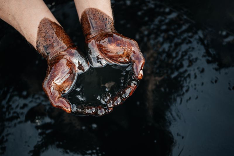 Hands are soaked in crude oil against the background of spilled petroleum