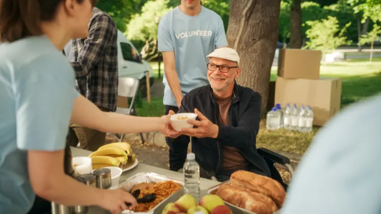 Group of Volunteers Helping in a Local Community Food Bank, Handing Out Free Food to People in Need in a Park on a Sunny Day