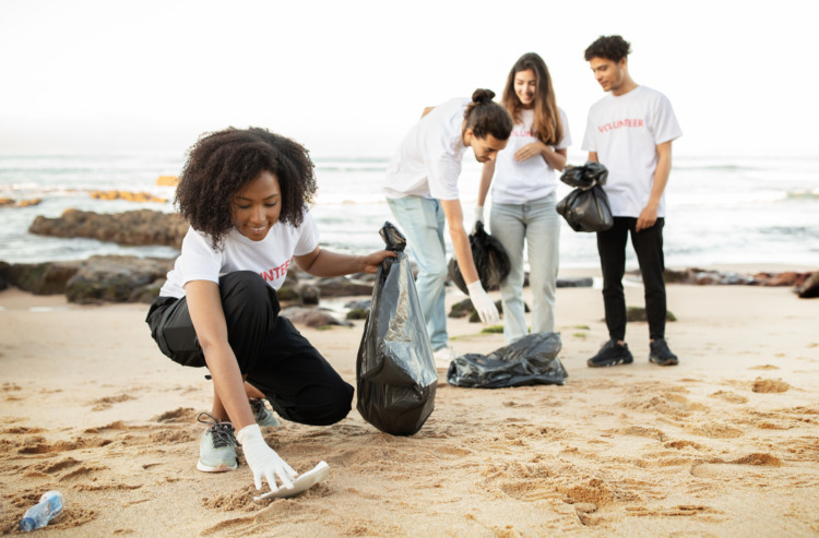 Happy young multiethnic people volunteers in t-shirts with garbage packages clean up garbage, plastic bottles