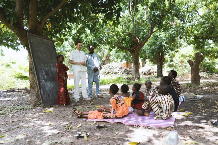 African teacher introducing a new white volunteer to a small group of destitute black schoolchildren in an open air classroom in a poor rural community