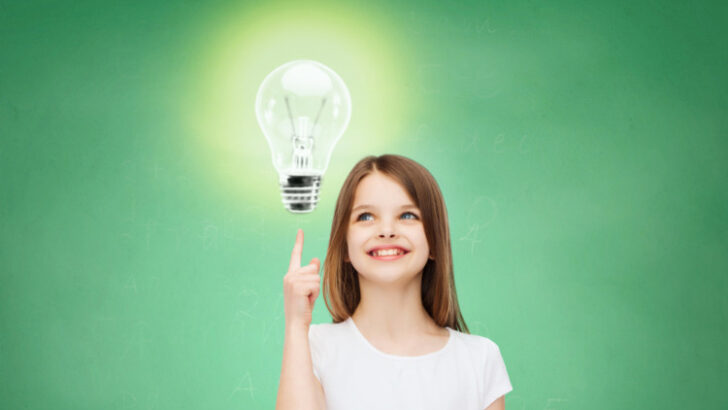 Smiling little girl in white blank t-shirt pointing finger up to light bulb