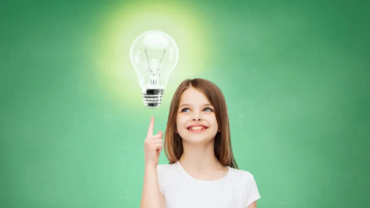 Smiling little girl in white blank t-shirt pointing finger up to light bulb