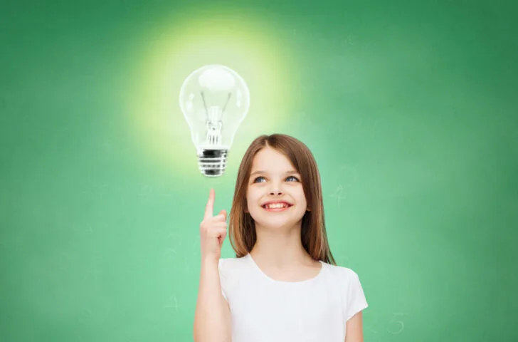 Smiling little girl in white blank t-shirt pointing finger up to light bulb