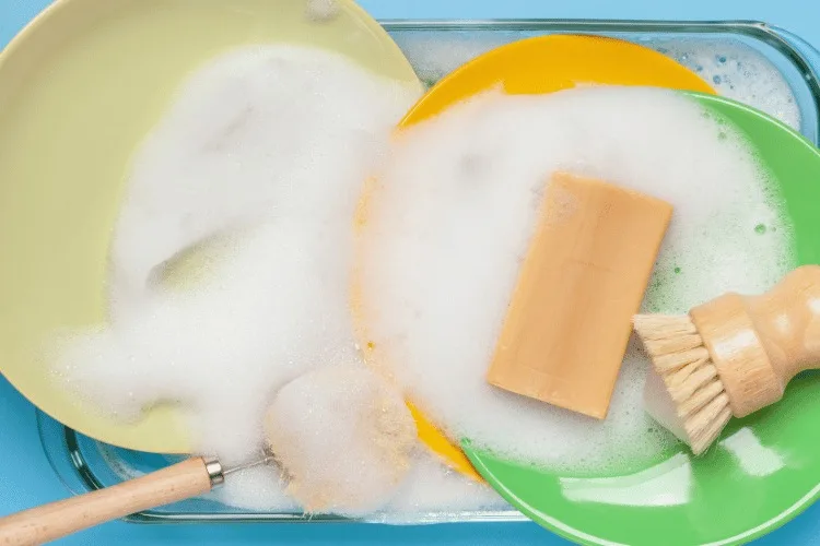 15 Best Zero-Waste Dish Soap Options 1 Washing dishes with zero waste soap foam plates and bamboo washing brushes