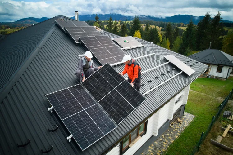 Men electricians in helmets installing solar panel system on the roof of a house