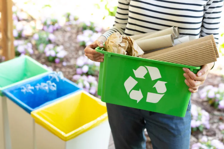 Close-up of a green basket with a recycling symbol with papers held by a woman