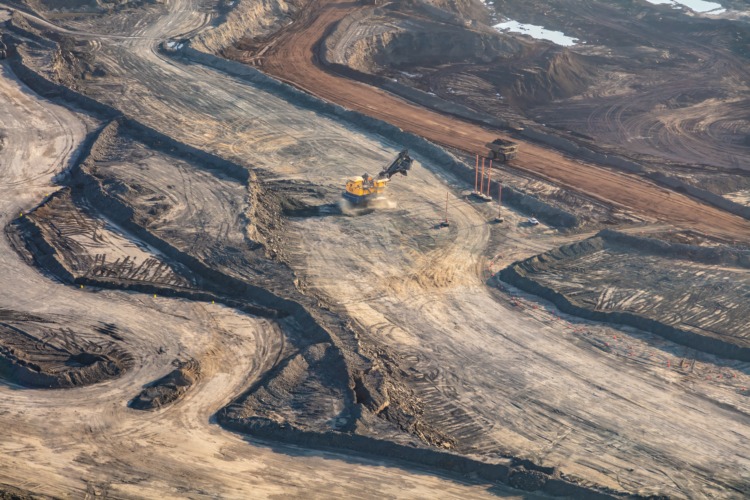 Aerial view of Canadian commercial excavator surface mining on site for Oilsands a giant dump truck loaded and heading to nearby refineries travel