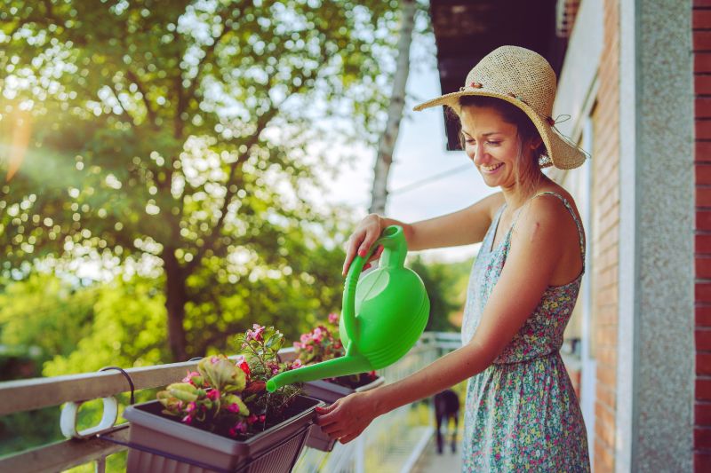 Young beautiful woman watering plants on her balcony garden