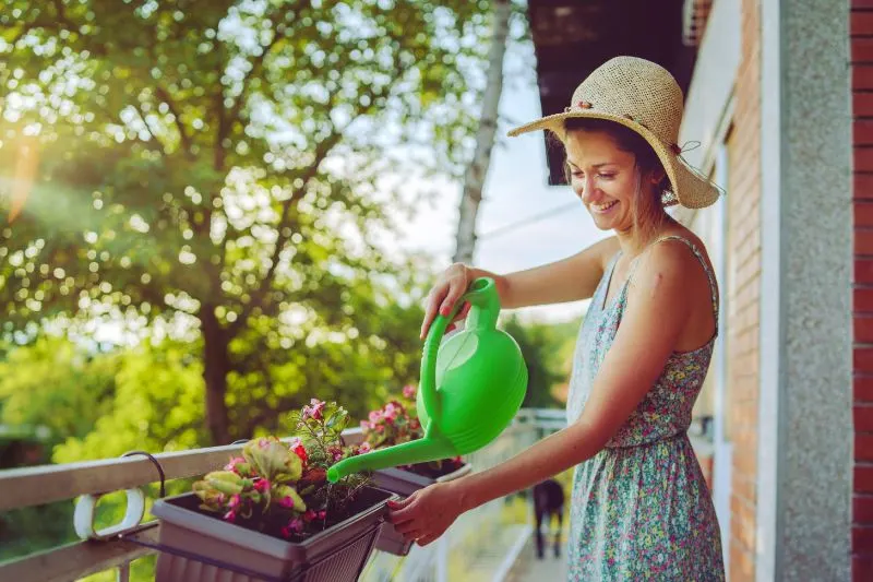 Watering plants on her balcony garden Young beautiful woman watering plants on her balcony garden