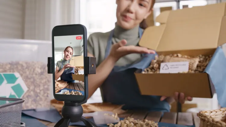 What Is Sustainability Content Marketing? Definition & Things to Know 1 SME owner go green net zero retail store live stream talk on phone showing eco care plastic free packaging box. Asia people young woman record video on tiktok IG reel instagram shop happy side hustle