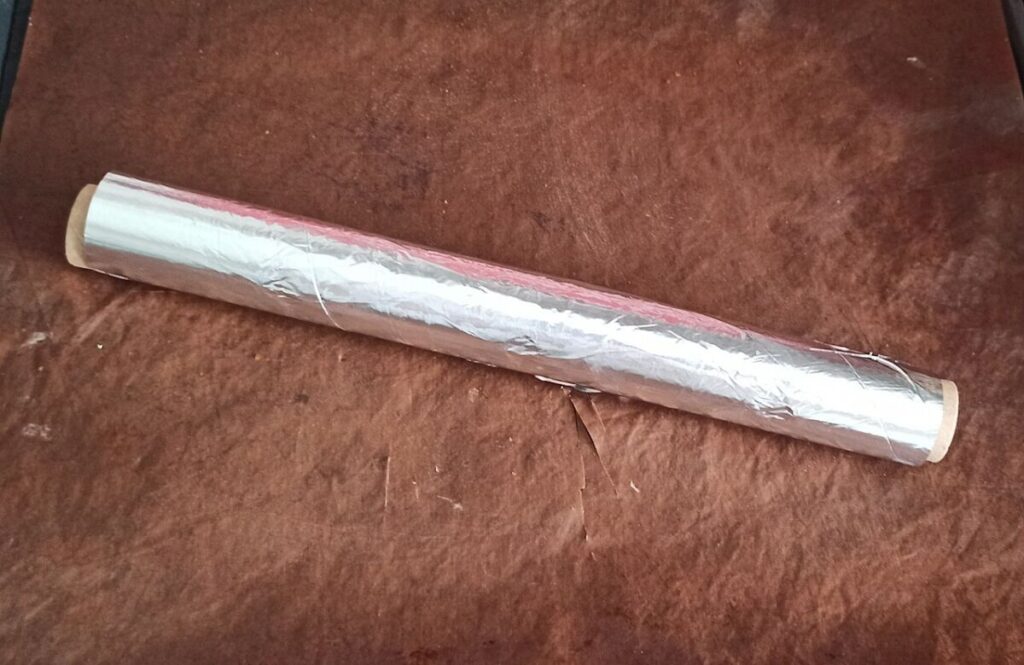 Is Aluminum Foil Recyclable? How to Recycle It Correctly 11 Roll of aluminum foil resting on a brown surface, highlighting its reflective surface and cylindrical shape.