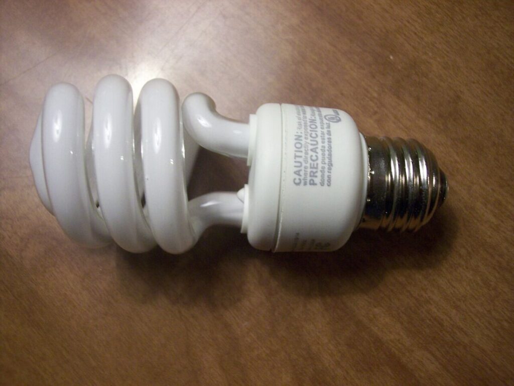Do Energy-Efficient Light Bulbs Give Off Radiation? 10 Compact fluorescent light bulb resting on a wooden table, showcasing its white color and unique shape.