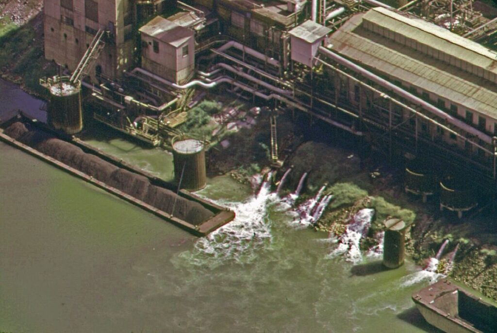 4 Types of Water Pollution: Sources, Effects, and Examples 17 Aerial view of a large industrial plant, showcasing smoke stacks and water discharge, highlighting industrial water pollution.