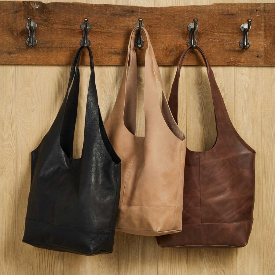 10 Best Fair Trade Handbags for 2026 21 Three leather Shilani slouch bags in umber color displayed on a wooden wall, showcasing their unique design and texture.