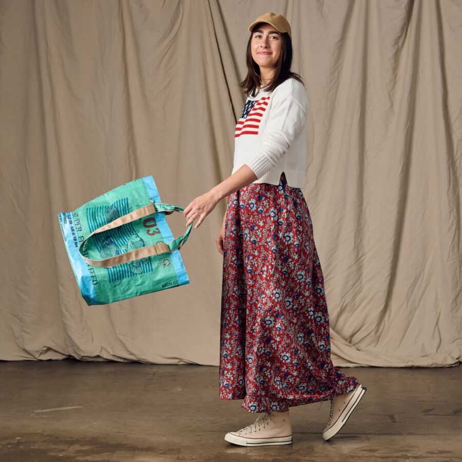 10 Best Fair Trade Handbags for 2026 15 Woman wearing a skirt and white shirt holds a large blue tote bag, showcasing the Trei design from Ten Thousand Villages.