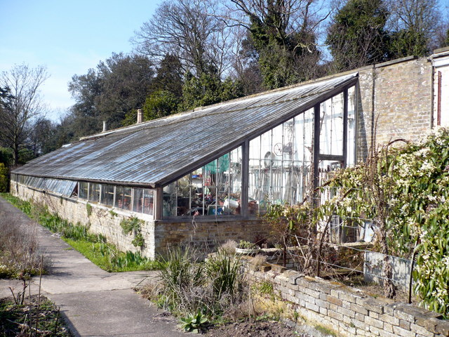 16 Best Lean-To Greenhouses for Small Yards & Side Walls 1 Victorian lean-to greenhouse featuring a glass roof and wooden frame, set against a garden backdrop.